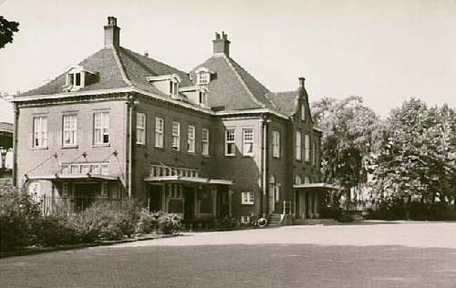 station Geldrop Straatzijde van het ingangsgebouw van station Geldrop.
<p>
Een bezoeker schrijft:<br>
<i>Achter het raam dat openstaat zat waarschijnlijk mijn oma uitkijkend over het spoor. Na het overlijden van haar man moest ze om haar weduwepensioen te behouden de de onbewaakte spoorbomen met de hand bedienen. Vaak met een baby op de arm, ze had 13 kinderen
en woonde boven de werkplaats, naast de perronchef. Ik zelf ben geboren in 1957 in dit gebouw toen mijn ouders hier nog inwoonden. Het is een grote schande dat dit gebouw voor een fietsenstalling en een telefooncel gesloopt moest worden.</i>