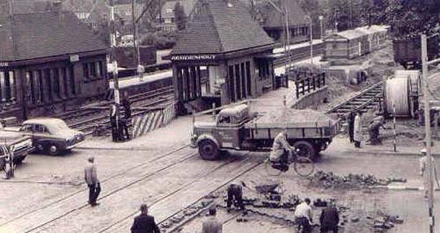 station Heemstede- Aerdenhout Straatzijde met spoorwegovergang. Duidelijk zijn er werkzaamheden zichtbaar. Mogelijk houden die verband met het omhoog brengen van het spoor waardoor de foto midden jaren '50 genomen zou moeten zijn.
<p>De aanleg van het dijklichaam voor de verhoogde spoorbaan is medio jaren 50 begonnen. Pas na 31 augustus 1957, toen de blauwe tramdienst was gestaakt konden de hulpsporen worden aangelegd. Vervolgens is het ontbrekende deel in het dijklichaam (waar de trambrug over het spoor ging, dit is iets ten zuiden van het huidige viaduct over de Westelijke Randweg)aangelegd. De hulpsporen waren iets naar het westen verschoven, waarbij na het gereedkomen van het viaduct over de Z.voorstelaan eerst Leiden-Haarlem hoog werd gereden, het lage hulpspoor Leiden-Haarlem werd toen afgebroken zodat er plaats was voor het afwerken van het viaduct zodat ook Haarlem-Leiden hoog kon worden gereden.
<p>Uiteindelijk is het gehele spoor iets oostwaarts verlegd, hetgeen te zien is als je naar de Leidse kant kijkt: het spoor buigt op het dijklichaam iets af, terwijl de oude lijn daar destijds kaarsrecht liep. Het is ook te zien aan de twee voorpleinen die sinds het nieuwe station veel duidelijker van omvang verschillen dan in de oude situatie.