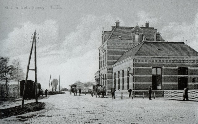 station Tiel ‘Station Hollands Spoor. Tiel.’ Is de titel van deze door de firma D. Mijs omstreeks 1910 uitgegeven ansichtkaart. Bij de voorkant van het stationsgebouw zijn op de bestrating van ‘kinderhoofdjes’ (natuurstenen keien van basalt), geen taxi’s te zien maar koetsjes. Links staat de Stoomtram van Tiel naar Buren en Culemborg gereed voor vertrek en op de achtergrond daarvan is nog net het fabriekscomplex te zien van de sucadefabriek van de fa. Udo. In het midden is de ook nu nog aanwezige overslagloods van de vervoersfirma van Van Gend & Loos te zien.