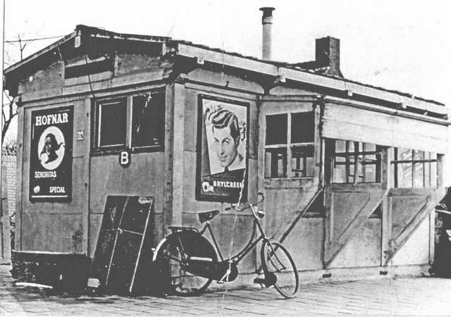 station Vierlingsbeek Op de foto staat een damesfiets, vermoedelijk van een van de paters Carmelieten uit Smakt,(oa mogelijk van. Pater Dionyus of Pater Jozef) die in Nijmegen op de Universiteit werkten of studeerden.
<P>
Onder bij de Hofnarreclame staat een pakket met oude of nieuwe te verzenden of aangekomen reclames voor vervanging in de lijst van de reclameborden.<P>
Achter het station staat het nieuwe woonhuis van de eerste (?) stationschef, naar mijn mening de heer van der Zee.
<P>
De foto is van medio 1955 (?)
<P>Bron: Bert Schmitz